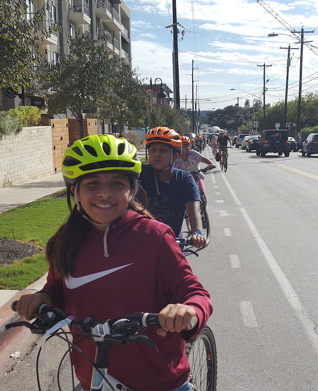 Long line of middle school aged cyclists in a bike lane.